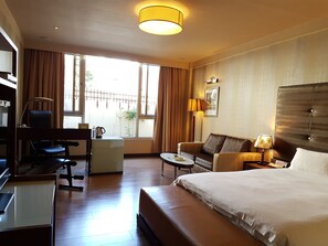 A hotel room with a bed, a sofa, a desk with a chair, a small table, and a lamp. - Gueylin Hotel (Taoyuan City)
