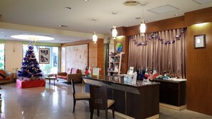 A hotel lobby with a reception desk, a Christmas tree, and a seating area with a couch and chairs. - Gueylin Hotel (Taoyuan City)
