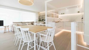 A modern kitchen with white cabinetry, a wooden dining table, and white chairs. - Brunet I | The Rentals Collection (San Sebastián)