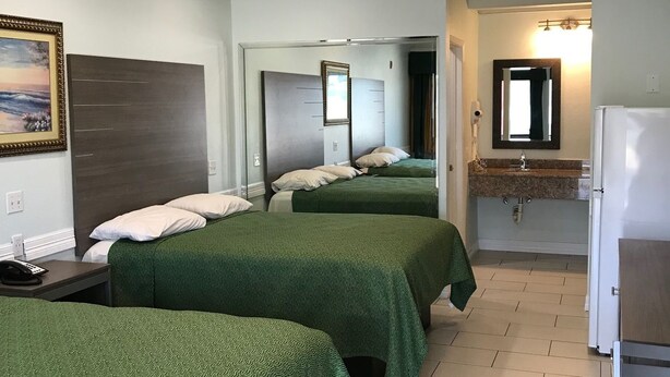 A hotel room with two beds, a small table, a bathroom with a mirror, and a ceiling light. - Crown Inn Humble (Humble)
