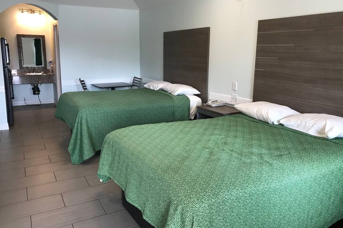 A hotel room with two beds, a small table, a chair, a mirror, and a sink.