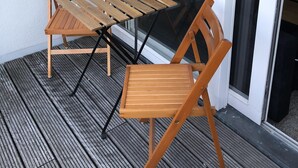 Une table en bois et deux chaises sur une terrasse en bois, avec une porte vitrée et une porte-fenêtre coulissante.