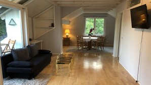 Un salon moderne avec un canapé foncé, une table basse en verre et un coin repas comprenant une table et des chaises.