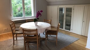 Un coin repas avec une table ronde, quatre chaises en bois, une nappe blanche et une orchidée en pot.