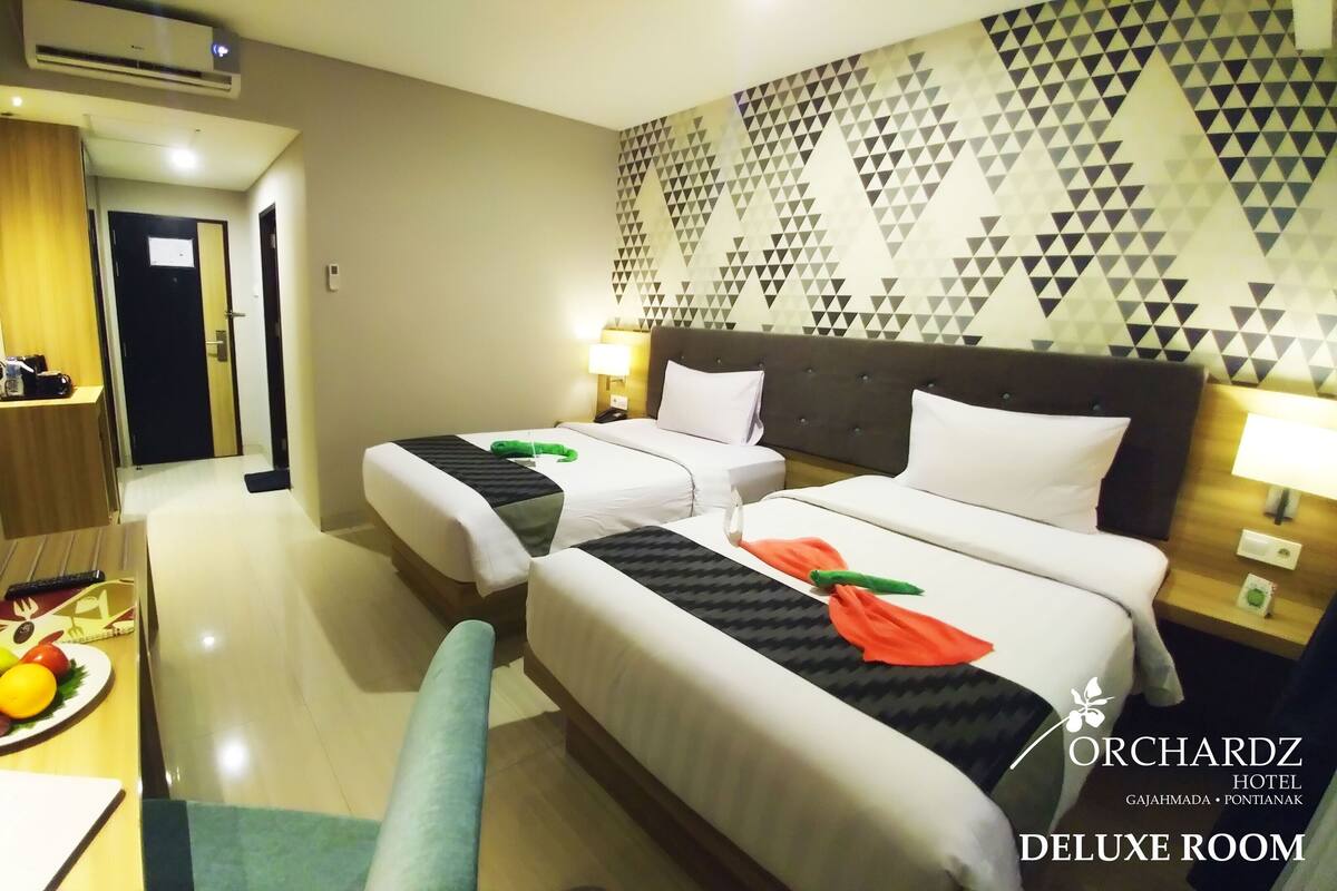 Una habitación de hotel con dos camas, una mesa de comedor con fruta y un adorno en la pared.