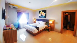 Une chambre d’hôtel avec un lit, des tables de chevet, un bureau avec un ordinateur portable, une chaise et une porte.