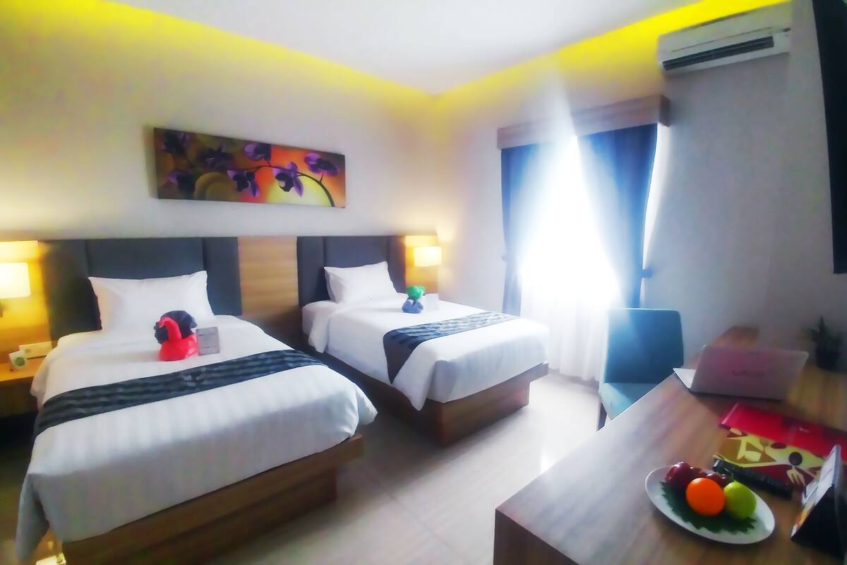 Habitación de hotel con dos camas, un escritorio, una silla, un televisor y un cuadro en la pared.