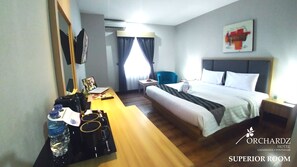 A hotel room with a bed, a desk with a laptop, a chair, a bedside table, and a water bottle. - Orchardz Hotel Gajahmada Pontianak (Pontianak)