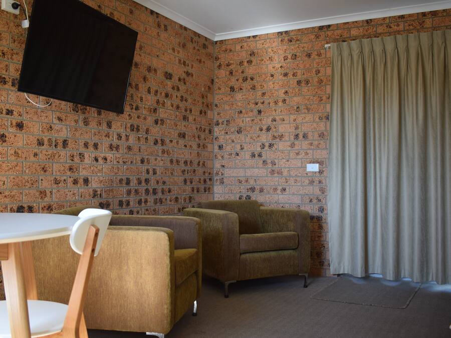 Et værelse med en væg i murstensmønster, et hvidt bord, to lænestole og en beige gardin.