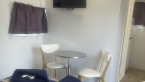 A small, neatly arranged room with a bed, two chairs, a round table, and a flat-screen TV mounted on the wall. - Bega Caravan Park (Bega)