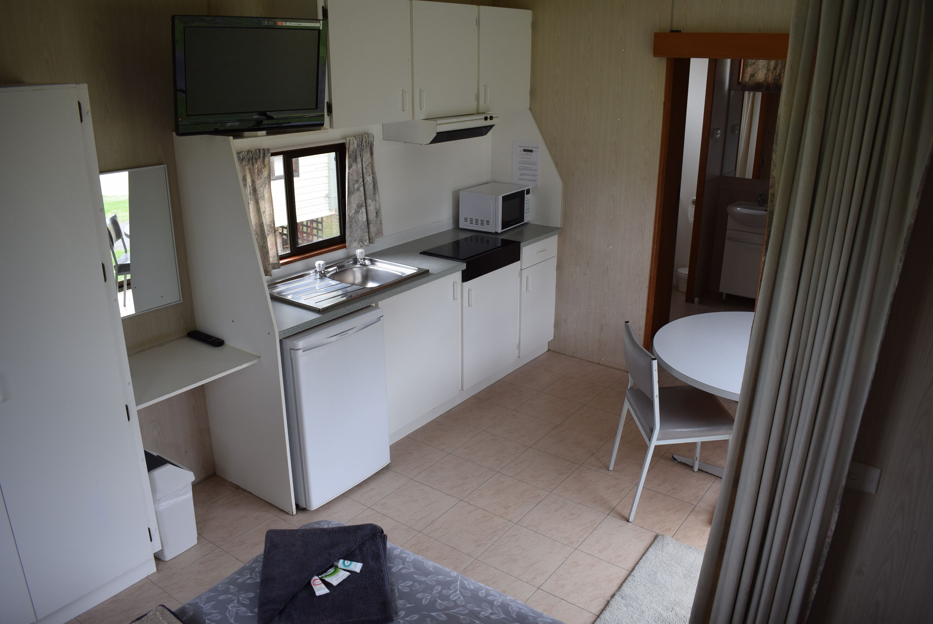 A compact kitchenette with a microwave, sink, and cabinets. There is a small dining table with a chair.
