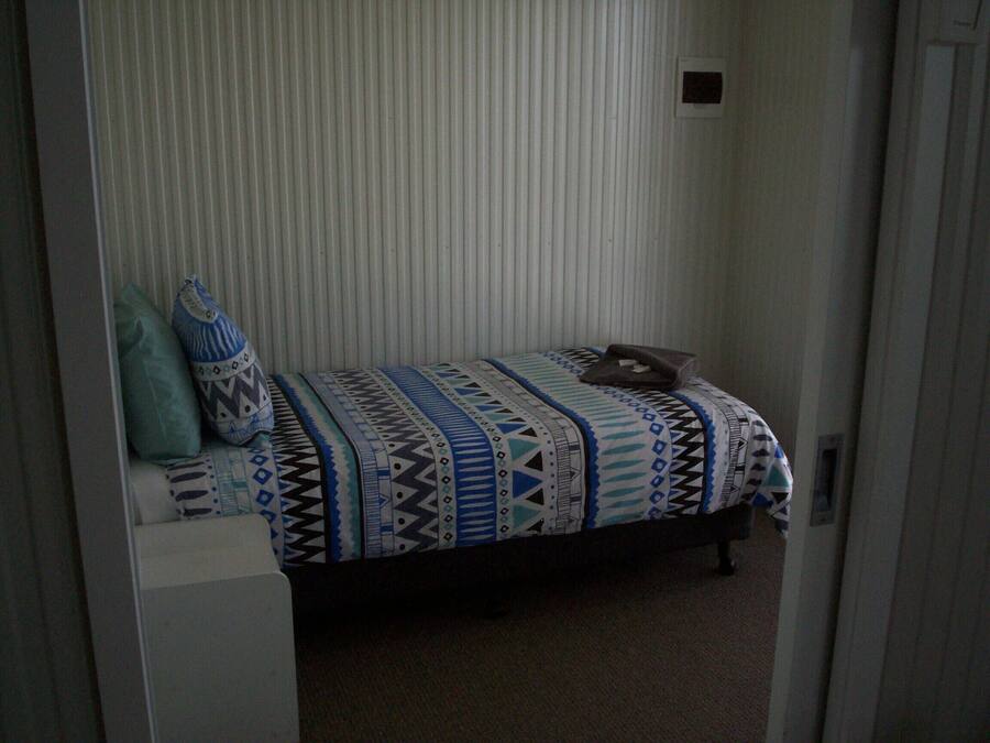 Una habitación pequeña con una cama individual, colcha estampada, almohada y mesita de noche.