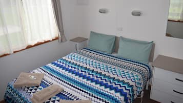 Ein Schlafzimmer mit einem Bett, zwei Nachttischen, einem Spiegel und einem Fenster mit Vorhängen.