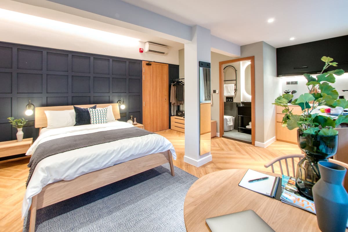 A modern hotel room with a large bed, a desk, and a view into the bathroom and kitchen.