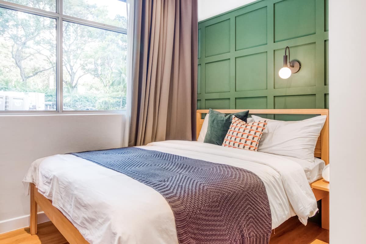 A neatly made bed with a patterned blanket, a green wall paneling, and a bedside lamp.