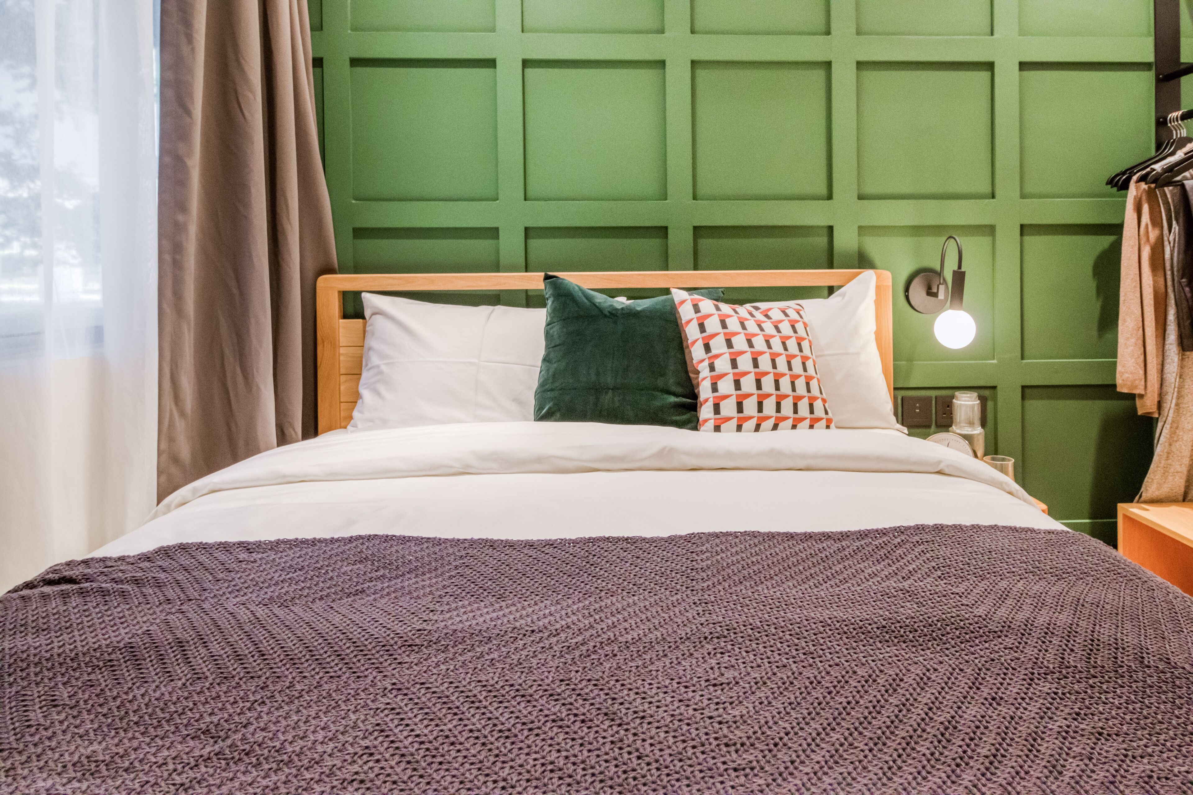 A neatly made bed with a white and purple blanket, a wooden headboard, and two pillows.