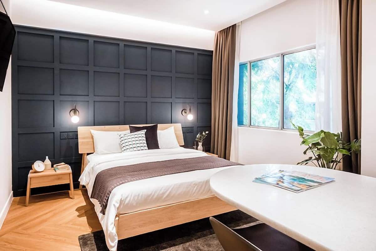 A bedroom with a bed, bedside table, lamp, window, and a table with a magazine.