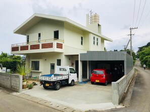 A two-story building with a flat roof, a balcony on the upper floor, and a garage attached to the right side.