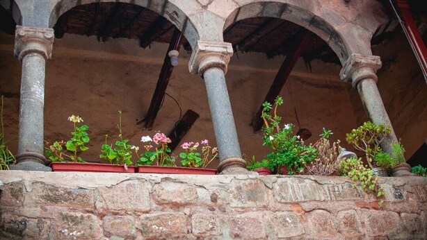 An outdoor area with stone columns and arches, potted plants, and a stone wall. - Hospedaje Laura (Cusco)