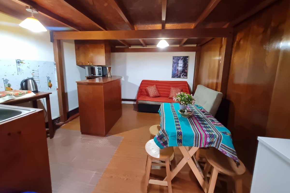 A cozy kitchen with wooden beams, a dining area with a colorful tablecloth, and a red sofa.