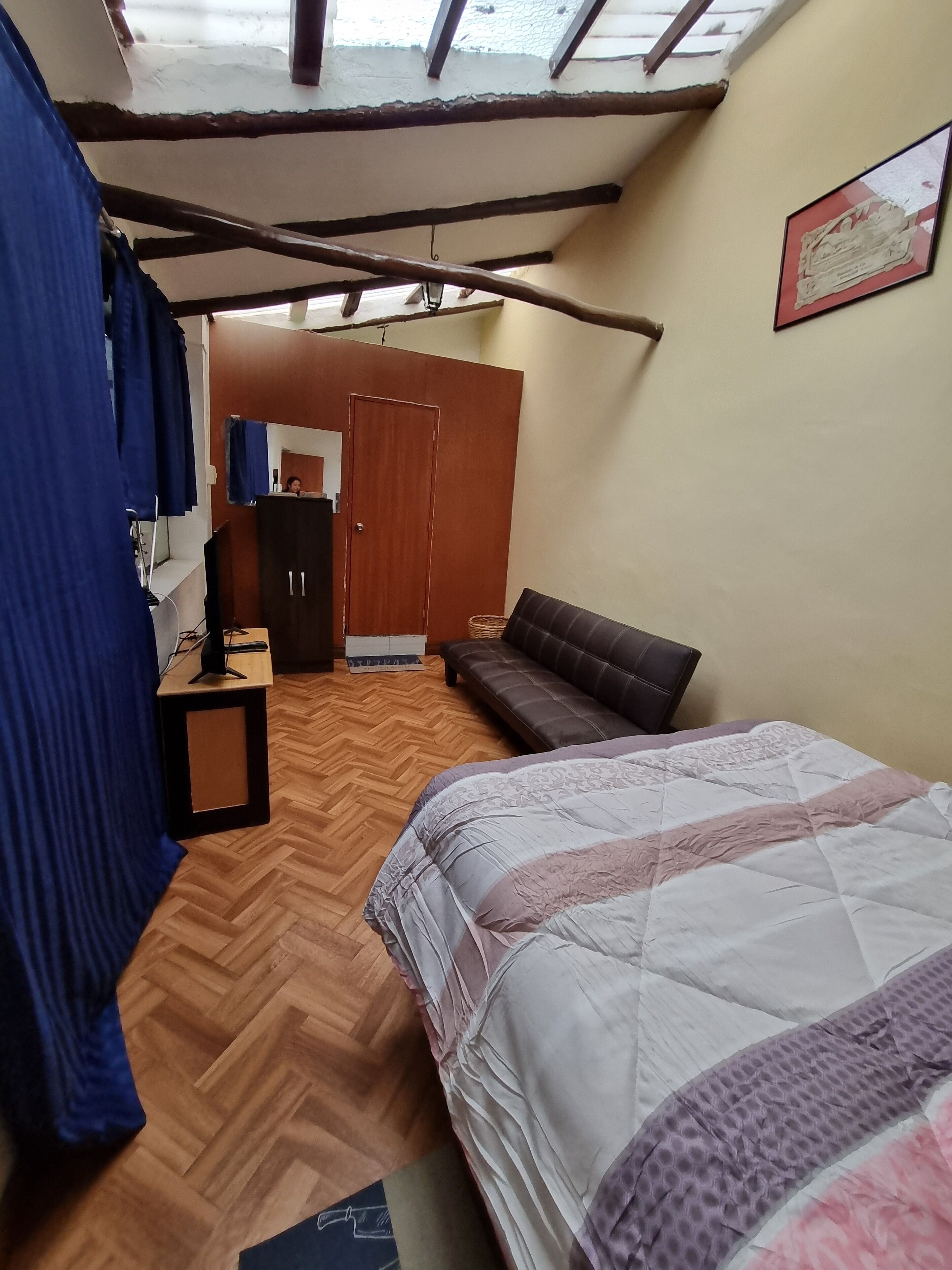A room with a bed, a sofa, a wooden herringbone floor, a wardrobe, and a mirror.