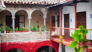 A traditional courtyard with stone arches, a red bridge, and potted plants. - Hospedaje Laura (Cusco)