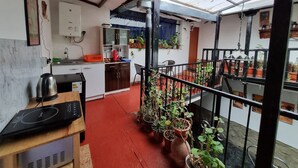 A compact kitchen with a sink, cabinets, and a countertop. There are potted plants and a dining area with a table and chairs. - Hospedaje Laura (Cusco)