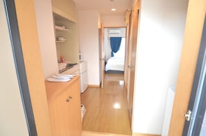 Un couloir étroit au plancher en bois, avec un réfrigérateur blanc et un four à micro-ondes posé sur un comptoir.