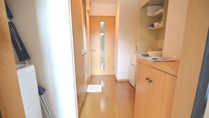 Een smalle gang met houten vloer, een witte radiator en een deur naar een andere kamer.