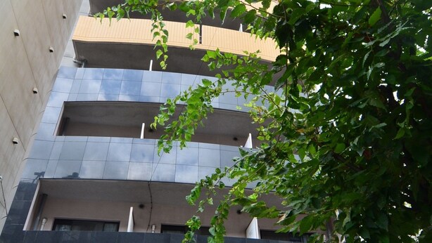 Een meerlaags gebouw met een oprit voor een parkeergarage, een rode auto daarbinnen en fietsen die er buiten staan.