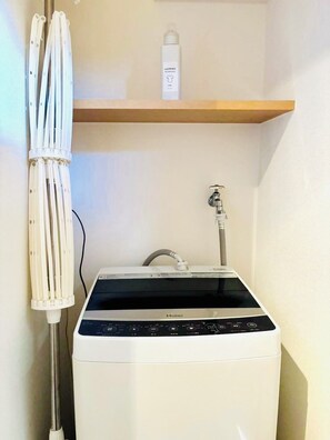 Une petite buanderie moderne, dotée d’un lave-linge et d’un sèche-linge à chargement frontal, d’une petite étagère avec une bouteille et d’un porte-serviettes blanc.