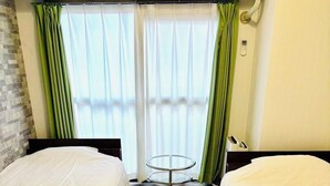 Een hotelkamer met twee bedden, een klein rond tafeltje en een raam met gordijnen.
