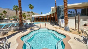 A swimming pool with lounge chairs and palm trees, surrounded by a building with a curved facade. - Mid-Century Modern Bohemian Bungalow w/ Pool (Palm Springs)