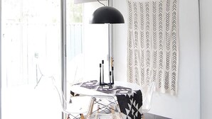 A modern dining area with a table, chairs, a black pendant lamp, and a patterned wall hanging. - Mid-Century Modern Bohemian Bungalow w/ Pool (Palm Springs)