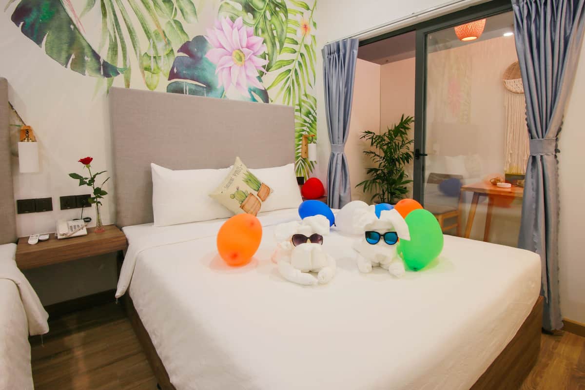 A hotel room with a large bed, a nightstand with a lamp, a wall with a floral mural, and a sliding glass door with curtains.