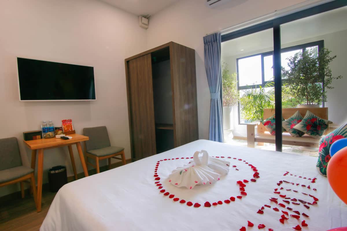 A hotel room with a bed, a TV mounted on the wall, a desk with chairs, and a view of the outdoors through a sliding door.