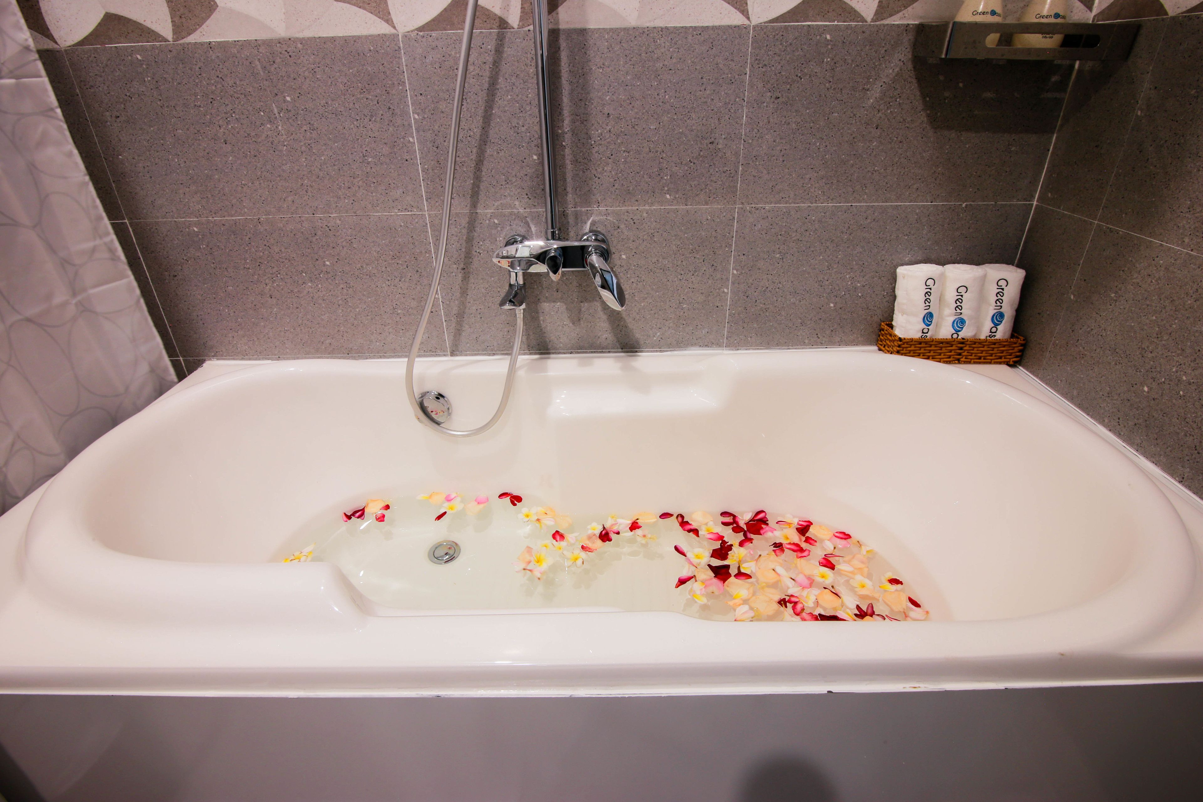 Une baignoire dans laquelle flottent des pétales de rose, une pomme de douche et un panier rempli de produits de toilette.