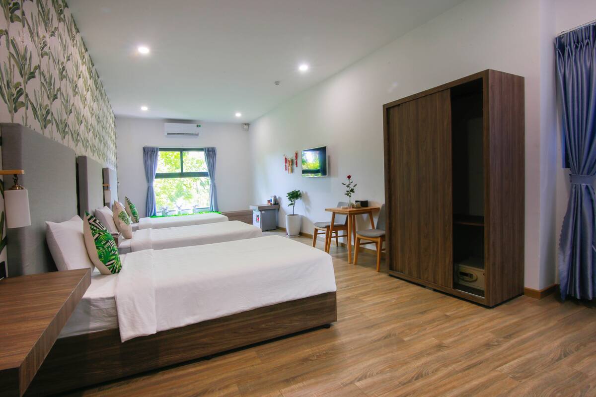 A hotel room with two beds, a desk, a wardrobe, a TV, and a window with curtains.