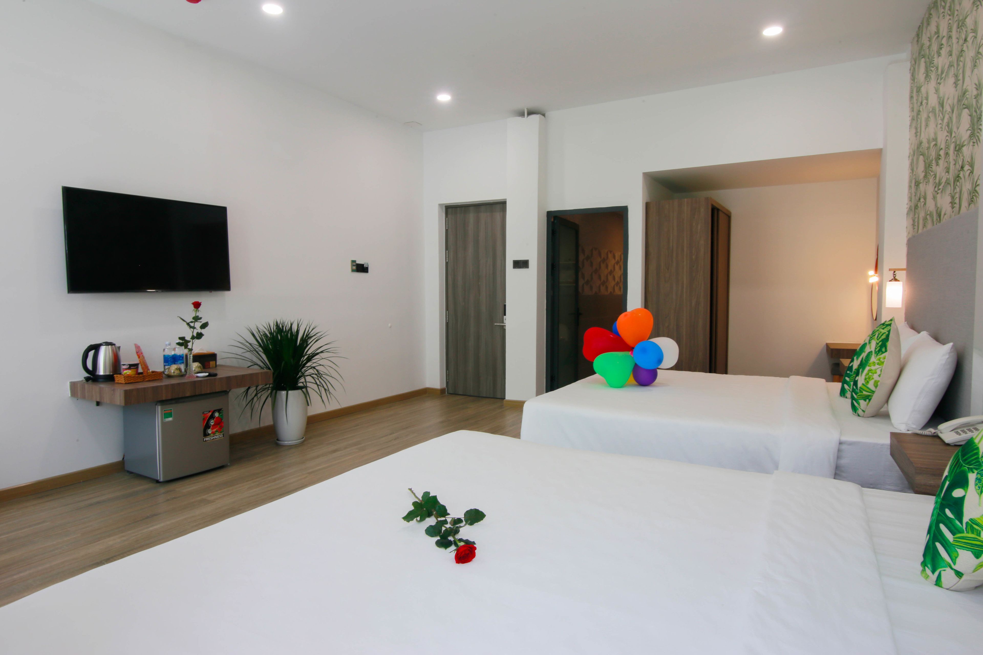 A hotel room with two beds, a TV, a small kitchenette, and a potted plant.