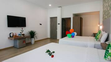 A hotel room with two beds, a TV, a small kitchenette, and a potted plant.