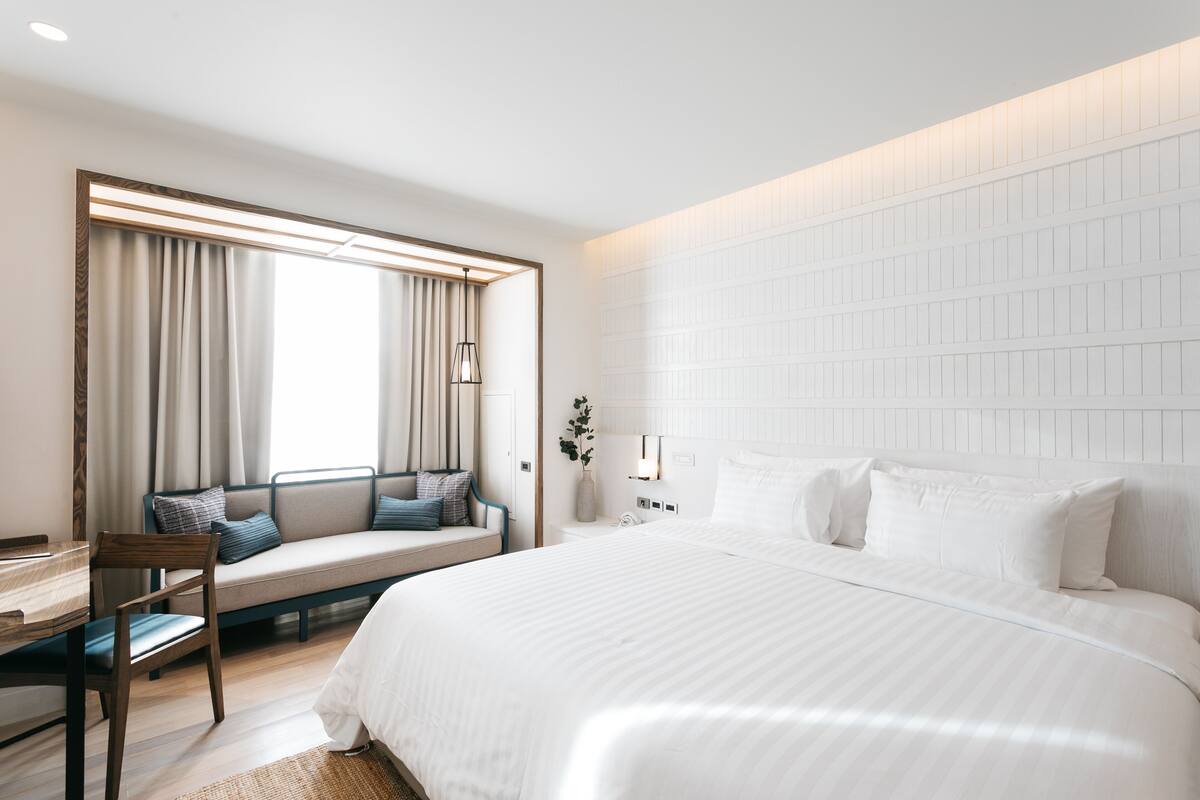Una habitación de hotel moderna con una cama grande, un área de descanso con vistas y un escritorio.