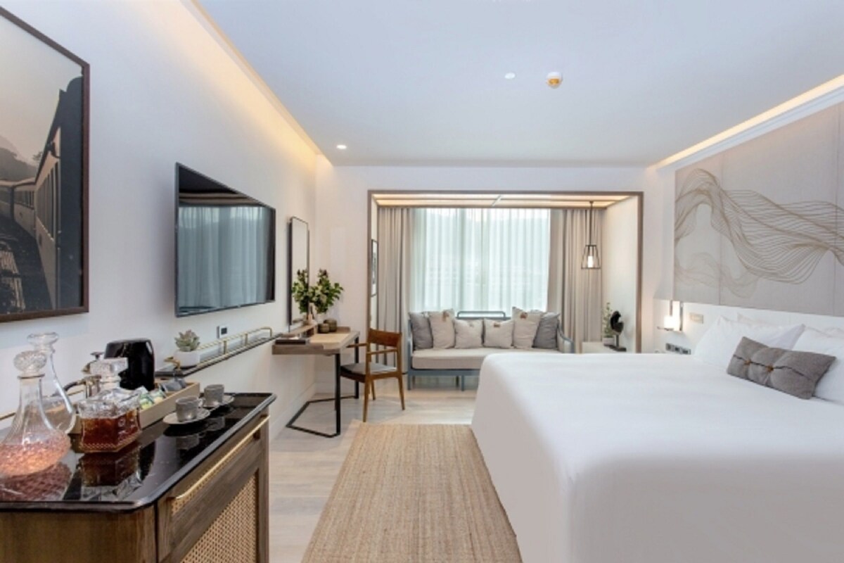 A modern hotel room with a large bed, a desk, and a seating area with a view of the city.