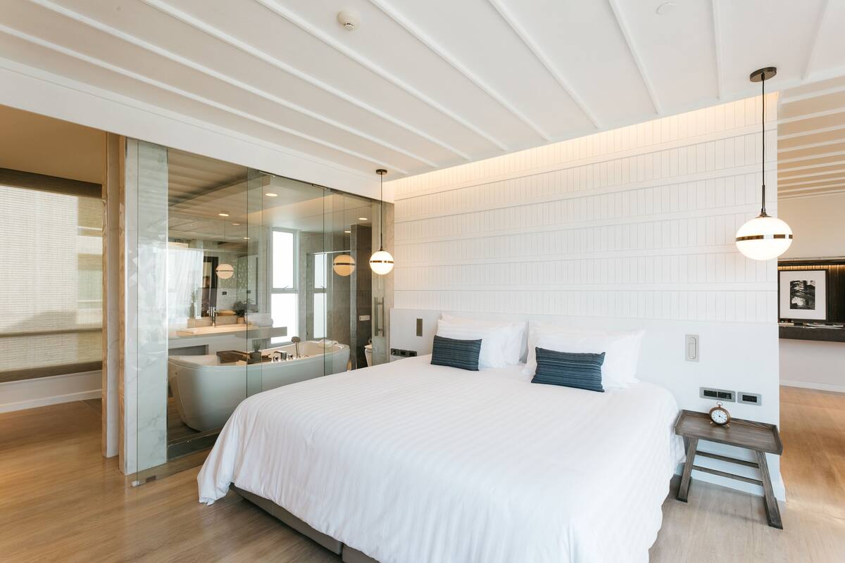 Un dormitorio moderno con una cama grande, cabina de ducha de vidrio y una mesita de noche de madera con un reloj.