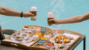 A breakfast tray with various food items and drinks, including croissants, eggs, and juice, placed by a poolside. - SYN Boutique Hotel (Chiang Mai)