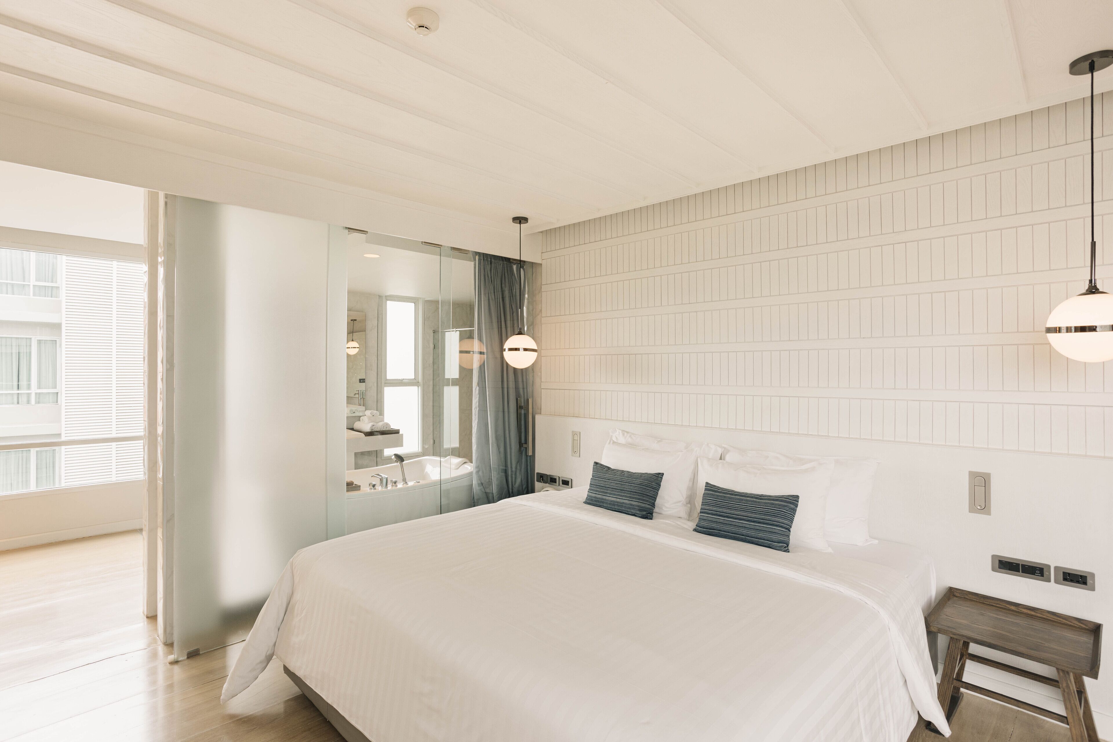 A modern hotel room with a large bed, a bedside table, a mirror, and a view of the city.