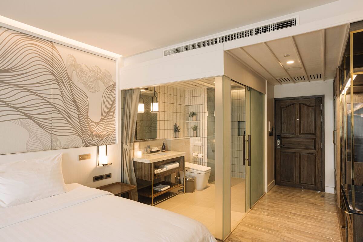 Una habitación de hotel moderna con una cama grande, un tocador con espejo, un inodoro y una zona de ducha.