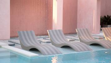 A pool area with three lounge chairs and a water feature.