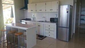 Una cocina moderna con armarios blancos, un refrigerador de acero inoxidable, un microondas y una estufa a gas. Hay dos taburetes en la isla.