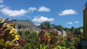 Un hotel con un área exterior techada, una escalera que sube a un nivel superior y abundante vegetación tropical.