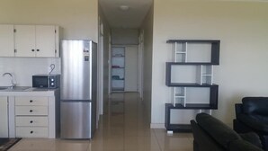 Una cocina moderna con refrigerador, microondas y lavamanos. Un pasillo conduce a una sala de estar con un sofá negro.